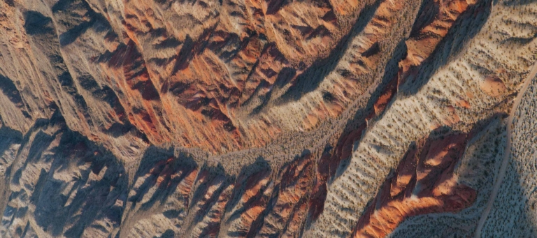 Eroded desert landscape with layered red and beige rock formations and sparse vegetation