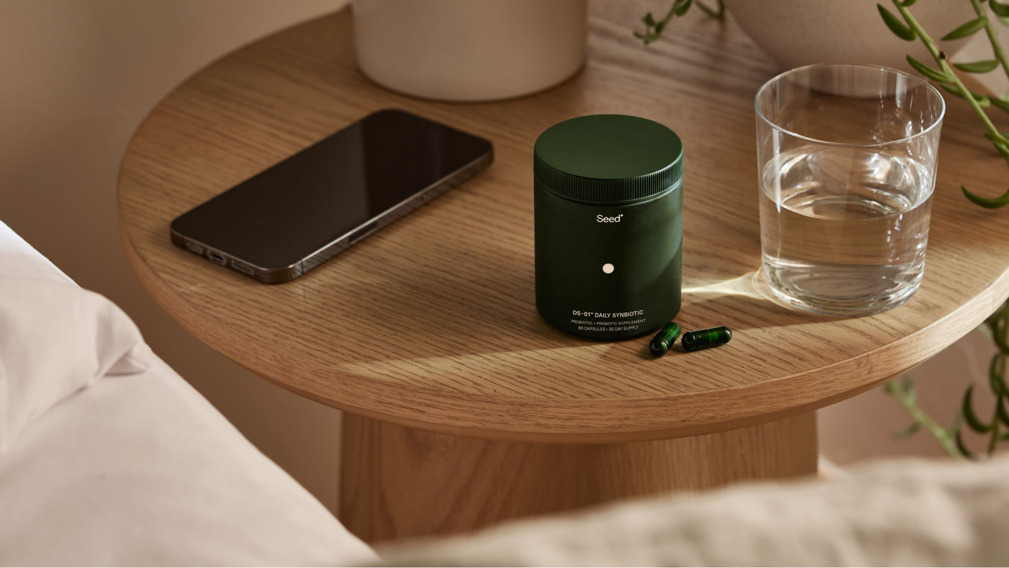 Smartphone, green supplement bottle with capsules, and glass of water on wooden table.