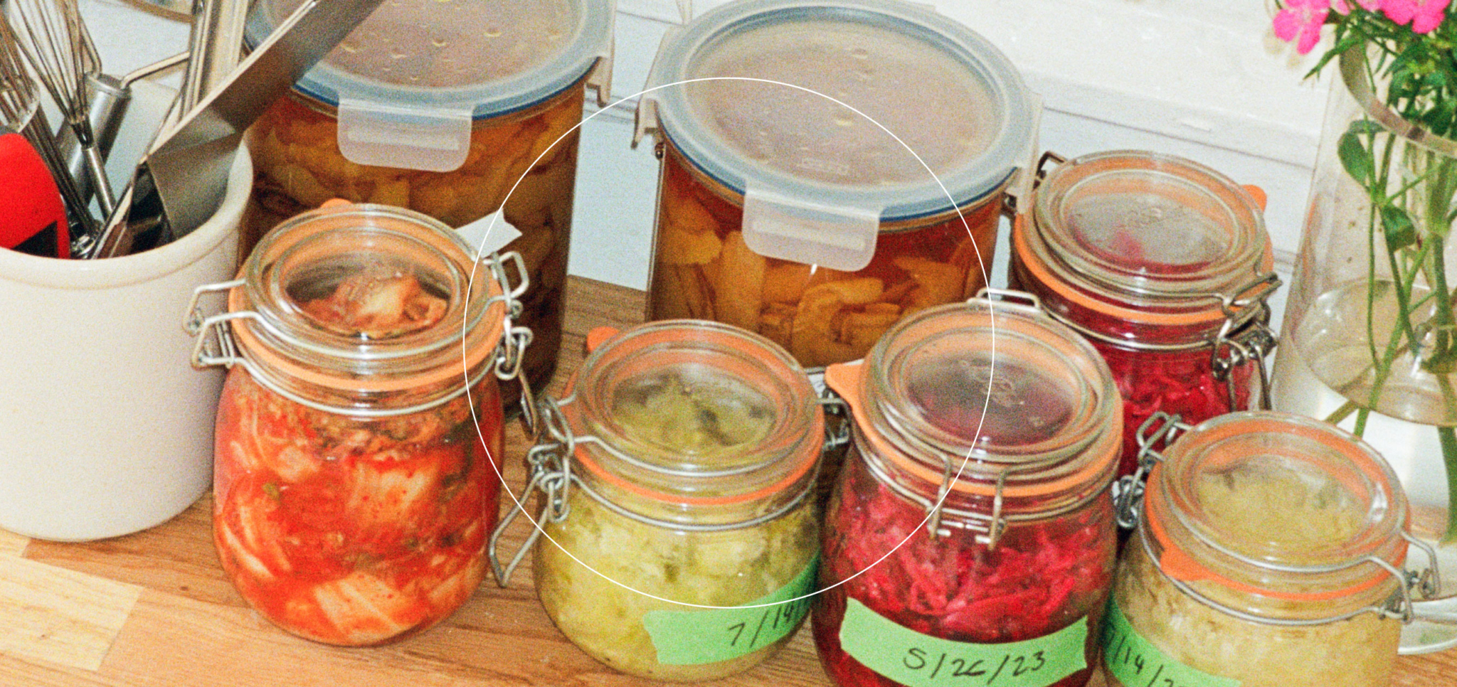 Glass jars filled with various homemade pickled vegetables on a wooden countertop.