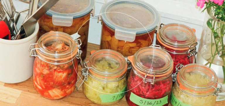 Glass jars filled with various homemade pickled vegetables on a wooden countertop.