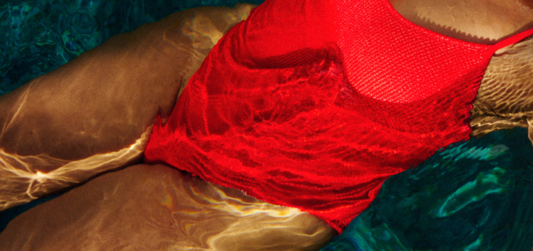 Person wearing a red swimsuit floating in clear water with light reflections on skin.