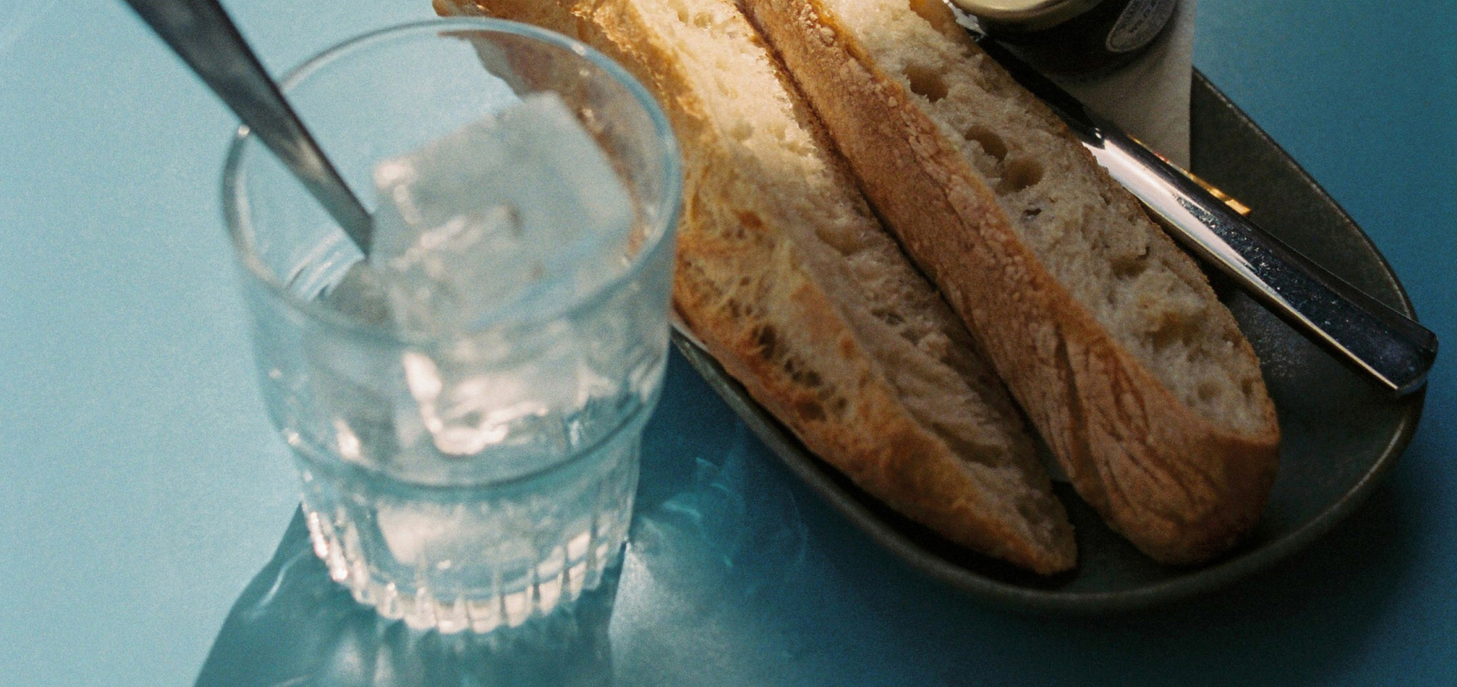 Glass of water with ice cubes and sliced baguette on a plate with a knife