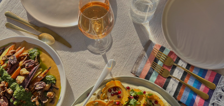 Table setting with roasted vegetable dishes, gold cutlery, and a glass of rosé wine