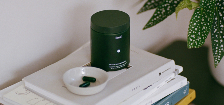 Black container of Med-Lock probiotic capsules on stacked books with a small dish holding two capsules.