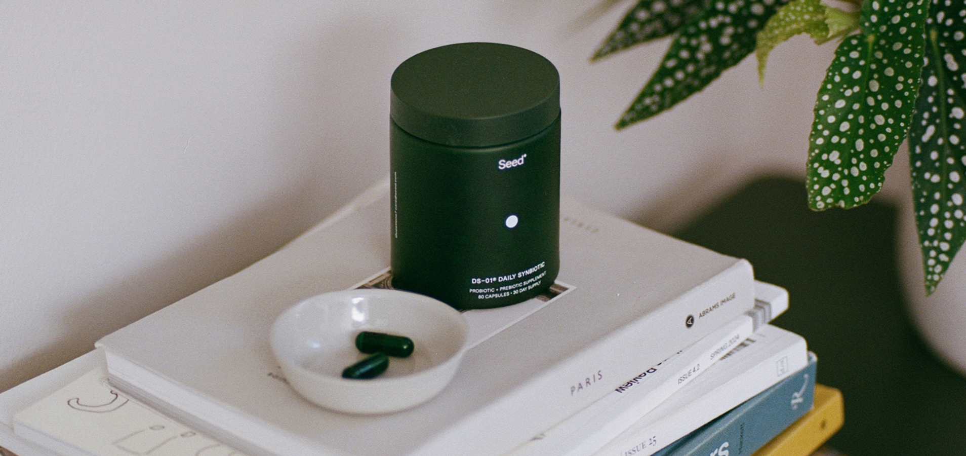 Black container of Med-Lock probiotic capsules on stacked books with a small dish holding two capsules.