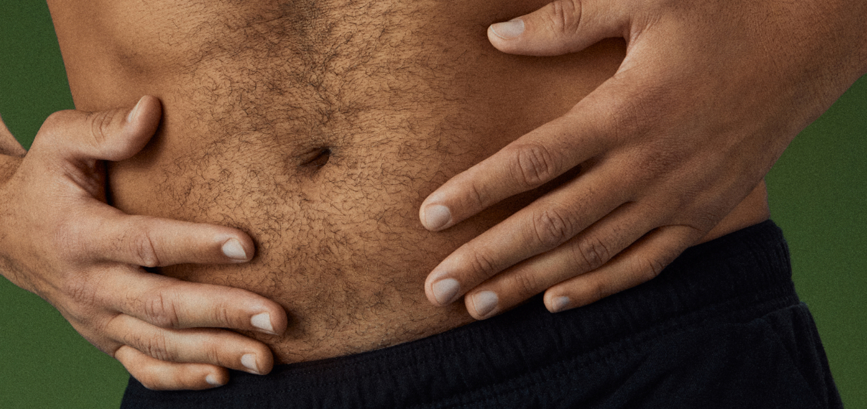 Close-up of a person holding their abdomen with both hands against a green background