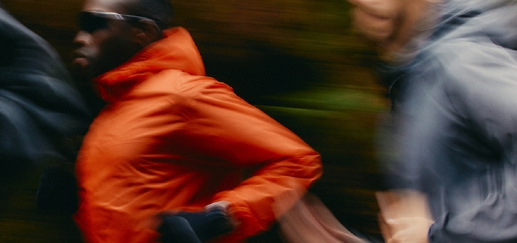 Three people running outdoors wearing jackets, motion blur effect.