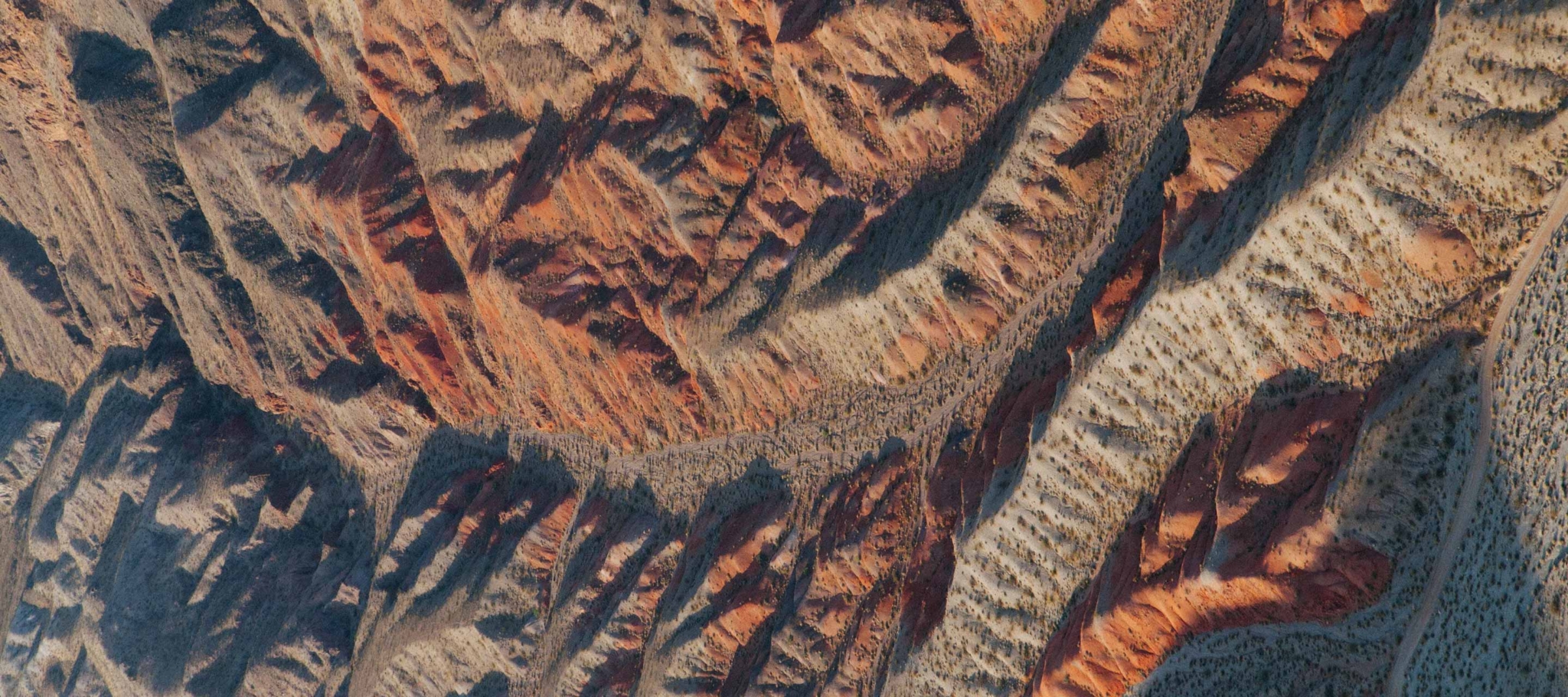 Eroded desert landscape with layered red and beige rock formations and sparse vegetation