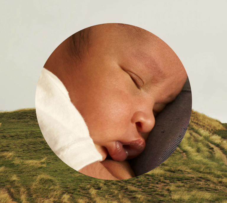 Infant sleeping in foreground with grassy hill in background