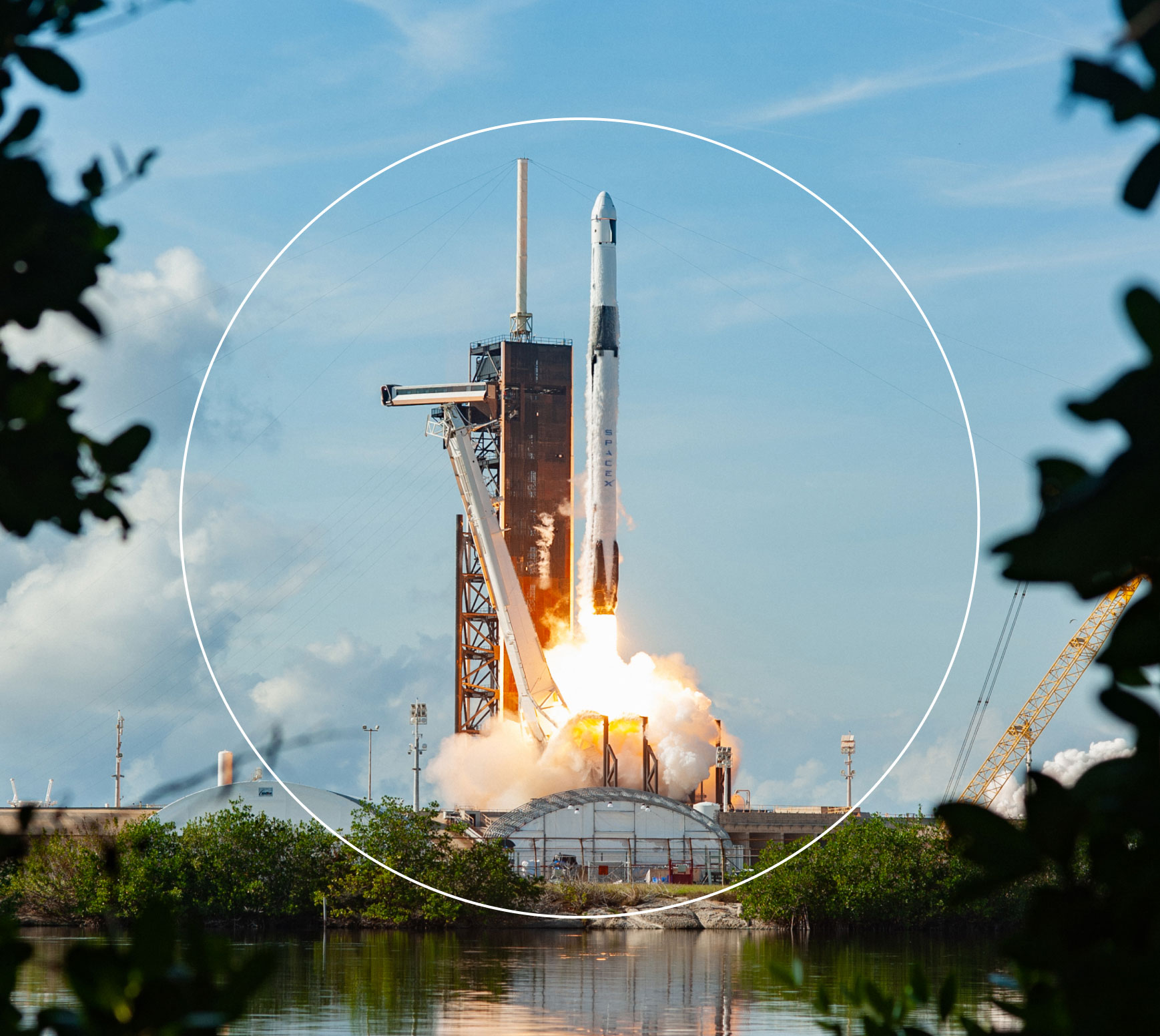 SpaceX rocket launching from a coastal launch pad with water and greenery in foreground.