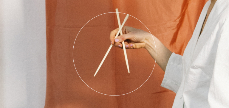 Hand holding wooden chopsticks against a two-tone fabric background
