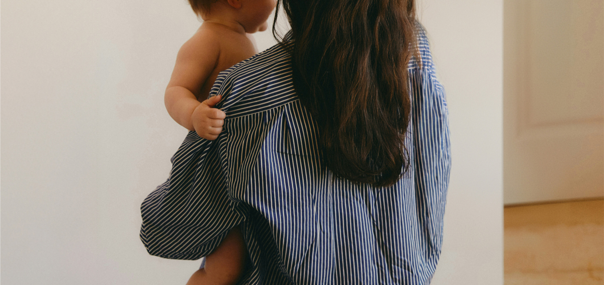 Woman with long hair holding a baby wearing a blue and white striped shirt indoors