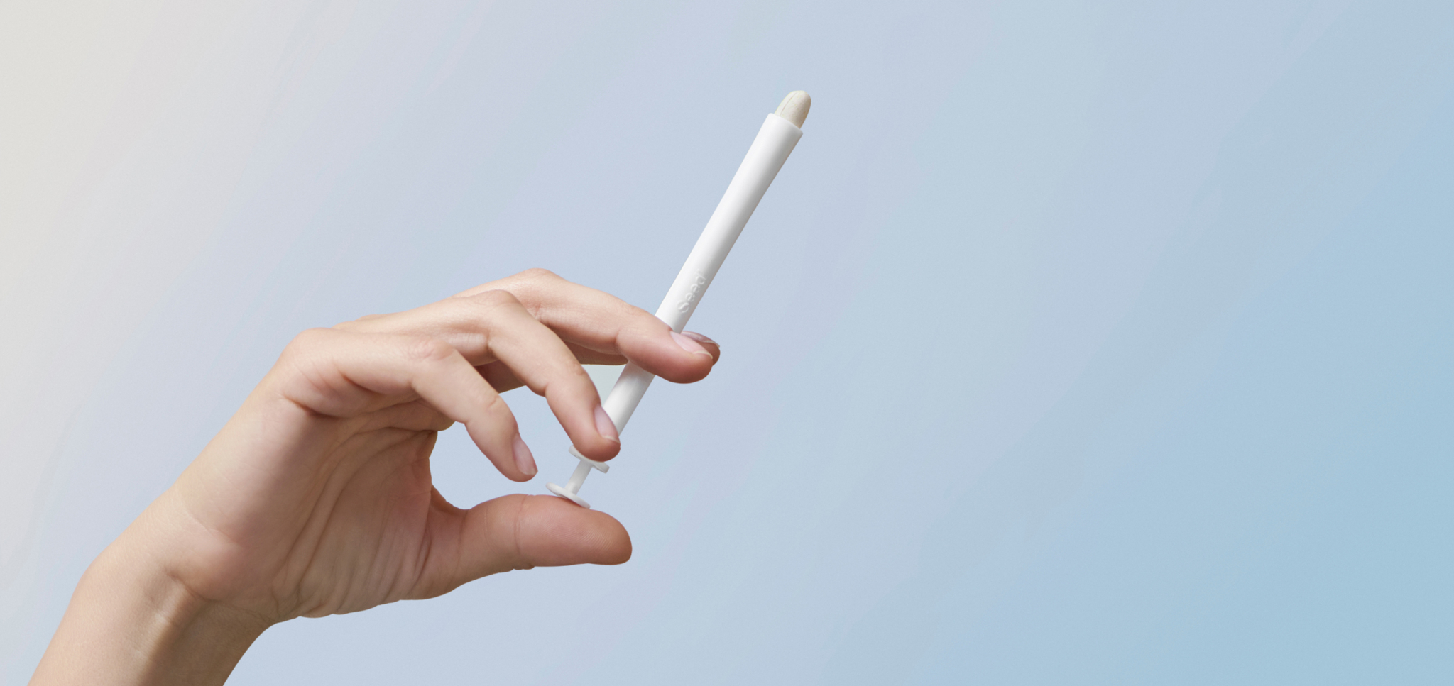 Hand holding a white applicator with a rounded tip against a blue background.