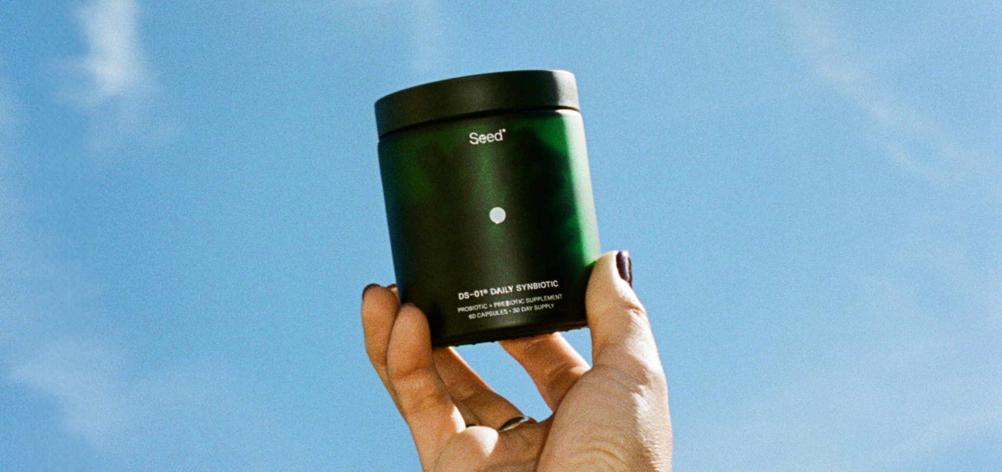 Hand holding a green container of Med-Lock DS-01 Daily Synbiotic supplement against blue sky.