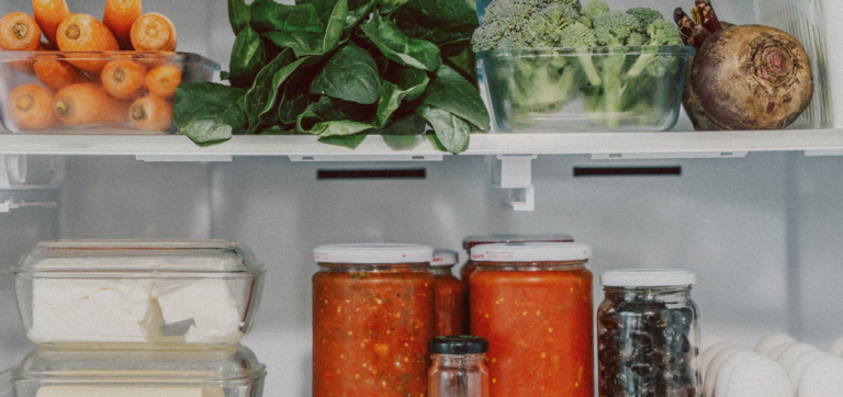 Fresh vegetables, jars of sauce, cheese, olives, and eggs inside a refrigerator.