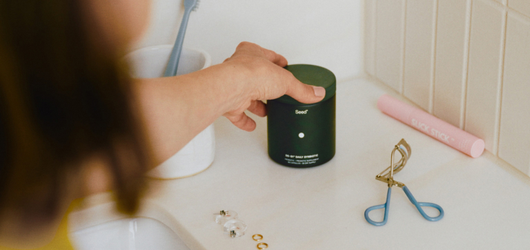 Hand reaching for a container of Med-Lock daily synbiotic on a bathroom counter with beauty tools.